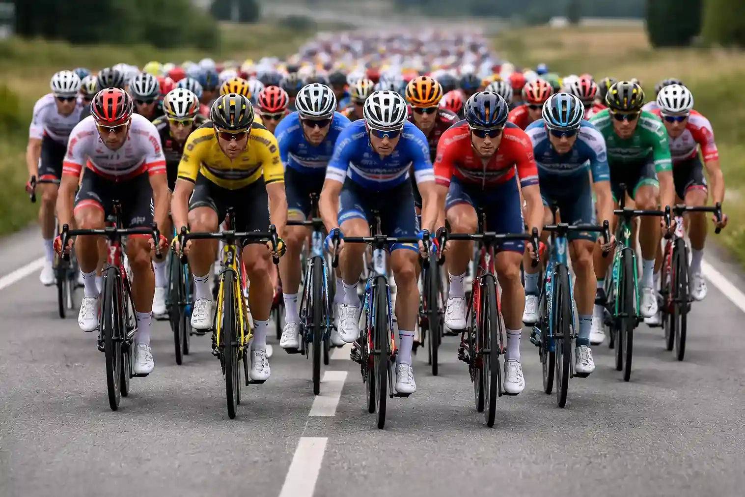 Primo piano di un ciclista professionista concentrato durante una corsa con il gruppo sullo sfondo