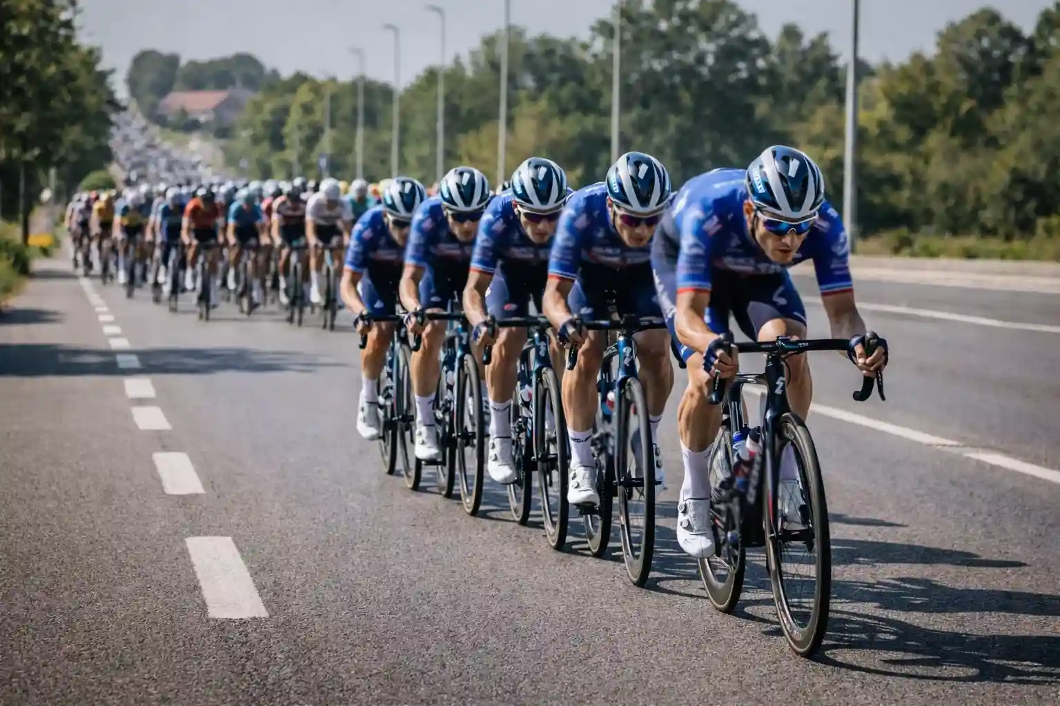 Squadra di ciclisti professionisti in formazione compatta che guida il gruppo in una tappa pianeggiante